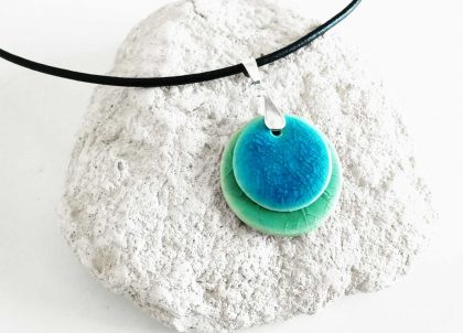 El Collar Disco Cristalino se caracteriza por la gran armonía que resulta de combinar  dos suaves tonos acristalados .  El esmaltado de estas finas piezas moldeadas con arcilla blanca y en forma de disco se realiza con un verde y  un turquesa que evocan el mar, tonos suaves muy Mediterraneos-